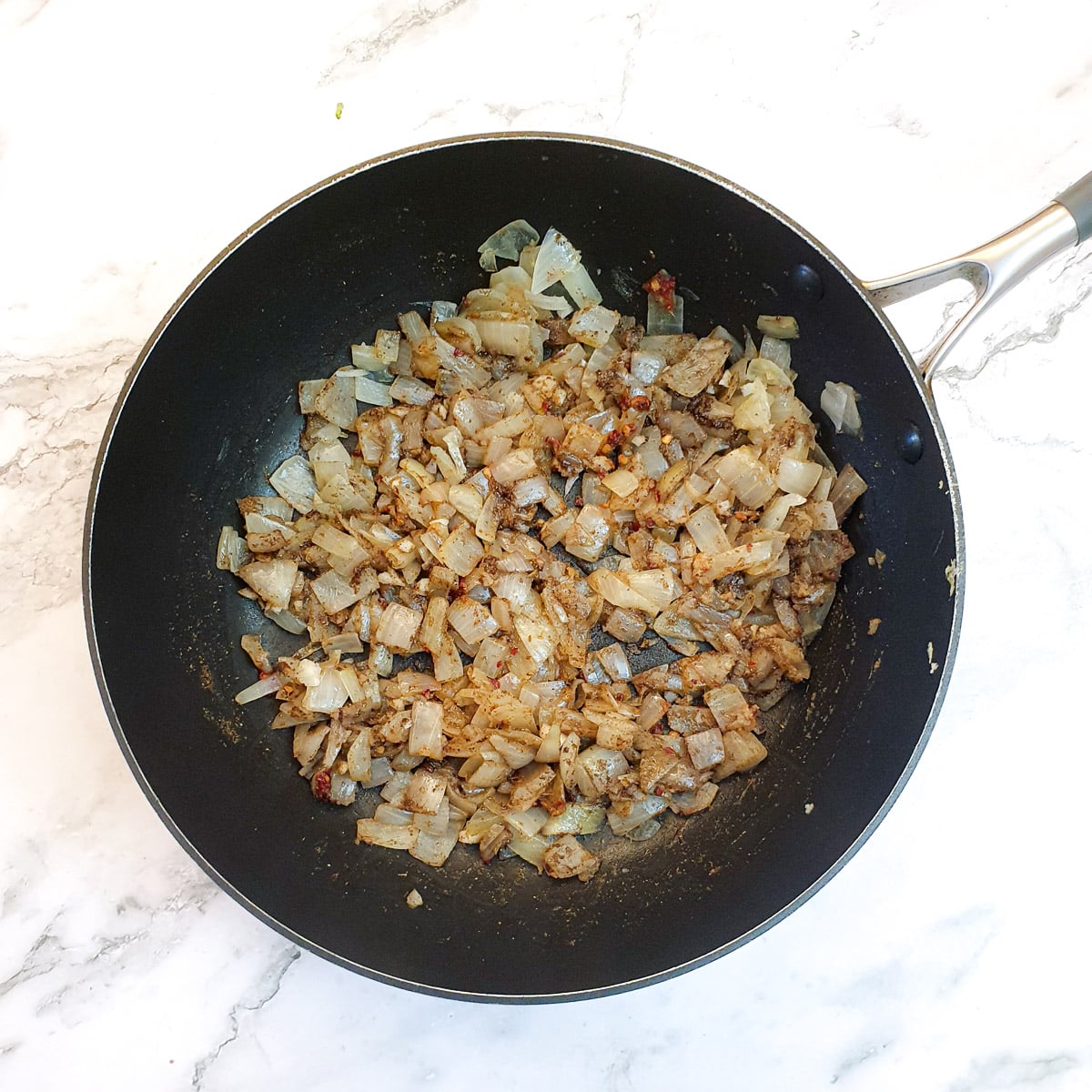 Chopped onions mixed with spices in a frying pan.