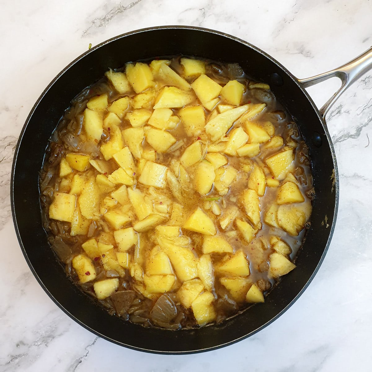 Chopped mango, vinegar and sugar added to the spicy onions in a frying pan.