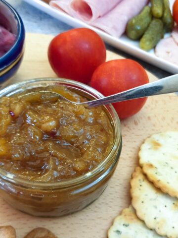 A jar of easy mango chutney served alongside a platter of meats and pickles.