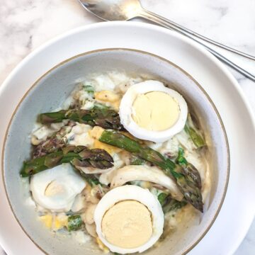 A dish of egg and asparagus salad garnished with additional sliced eggs amd asparagus spears.