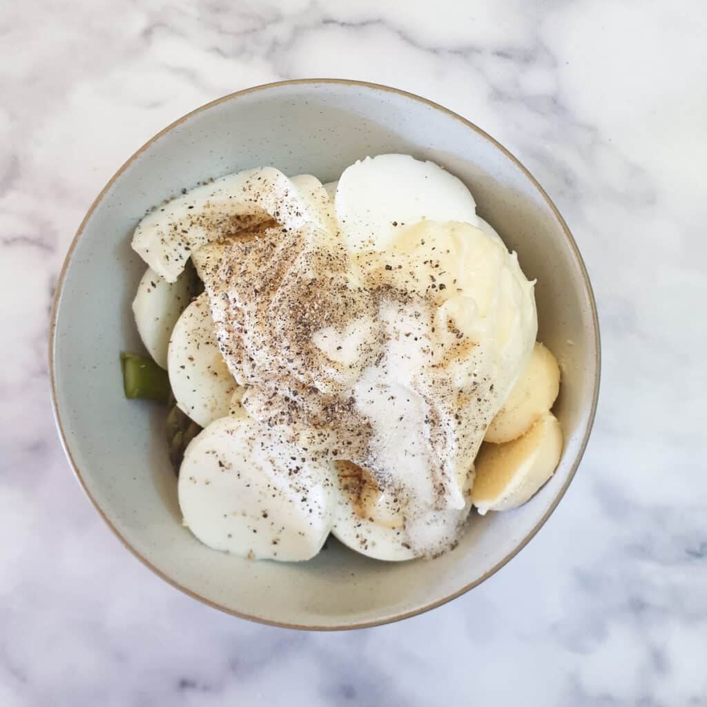 Asparagus, sliced eggs and mayonnaise sprinkled with salt and pepper in a mixing bowl.