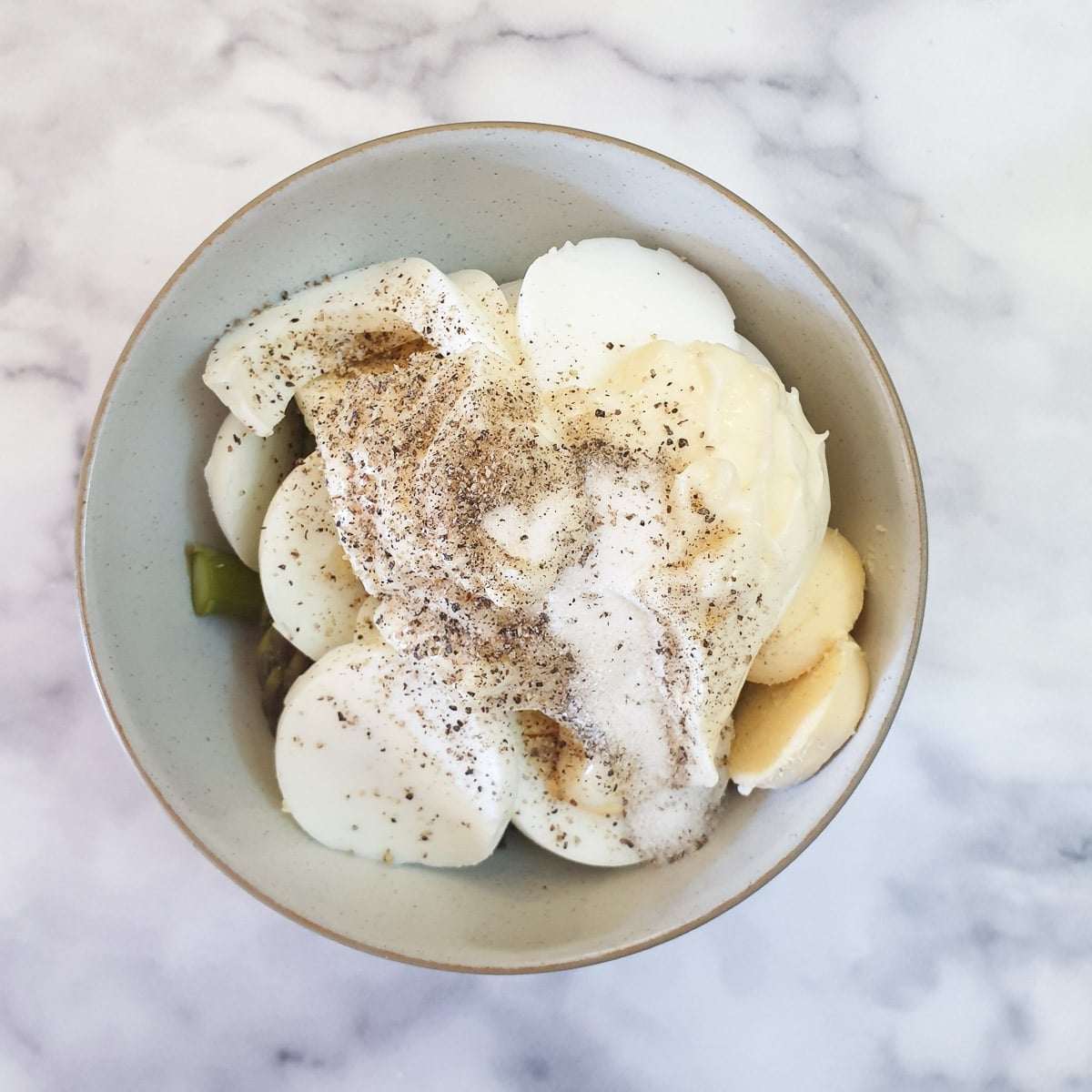 Asparagus, sliced eggs and mayonnaise sprinkled with salt and pepper in a mixing bowl.