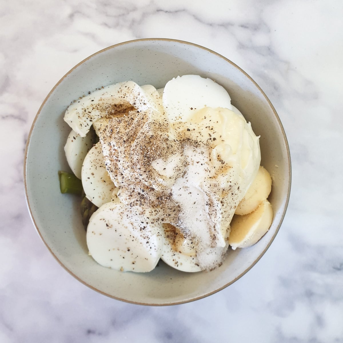 Asparagus, sliced eggs and mayonnaise sprinkled with salt and pepper in a mixing bowl.