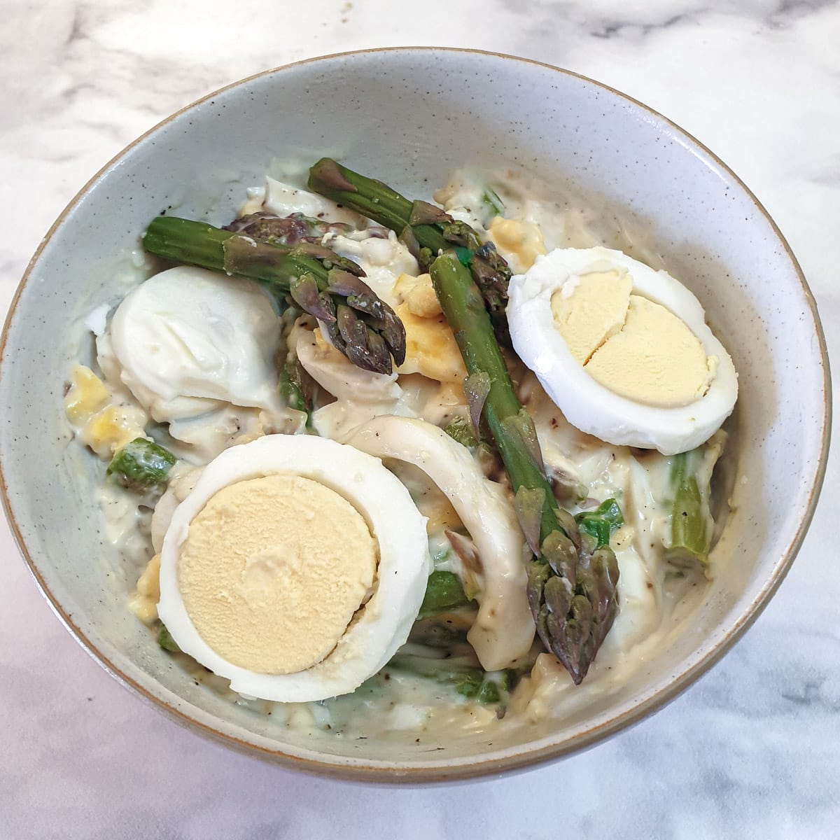 Slices eggs and asparagus spears on top of a dish of egg and asparagus salad.