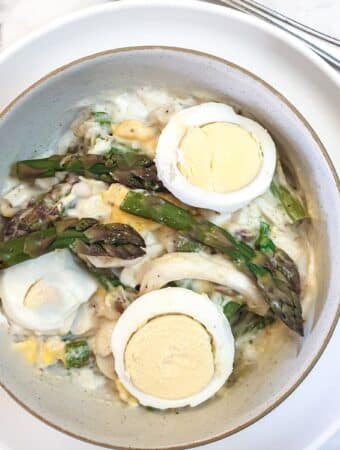 A dish of egg and asparagus salad garnished with additional sliced eggs amd asparagus spears.