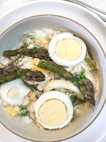 A dish of egg and asparagus salad garnished with additional sliced eggs amd asparagus spears.