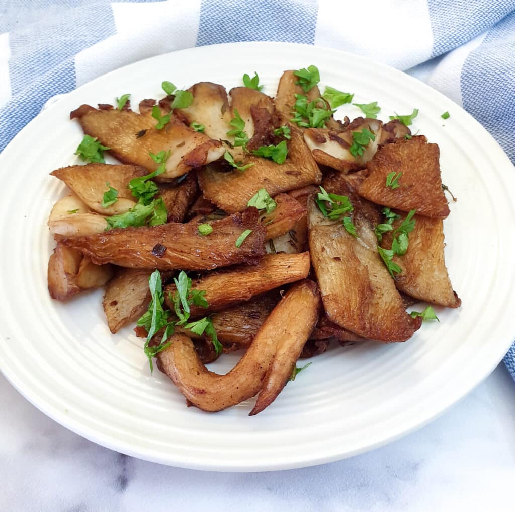A plate of browned oyster mushrooms garnished with chopped parsley.