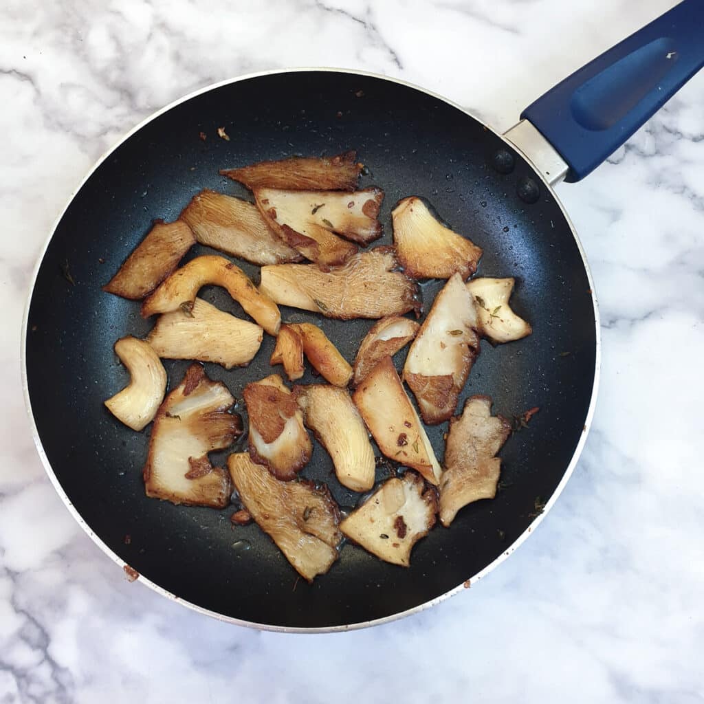 Browned slices of oyster mushrooms in a frying pan.