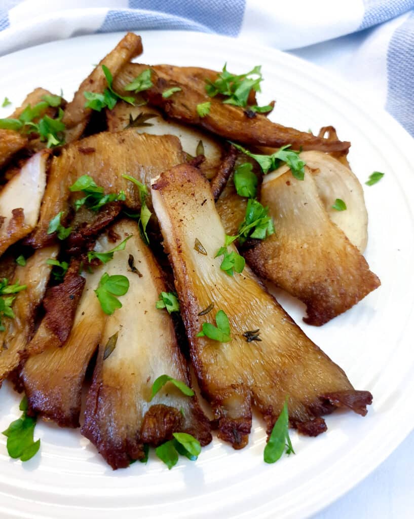 A plate of cooked oyster mushrooms garnished with chopped parsley.
