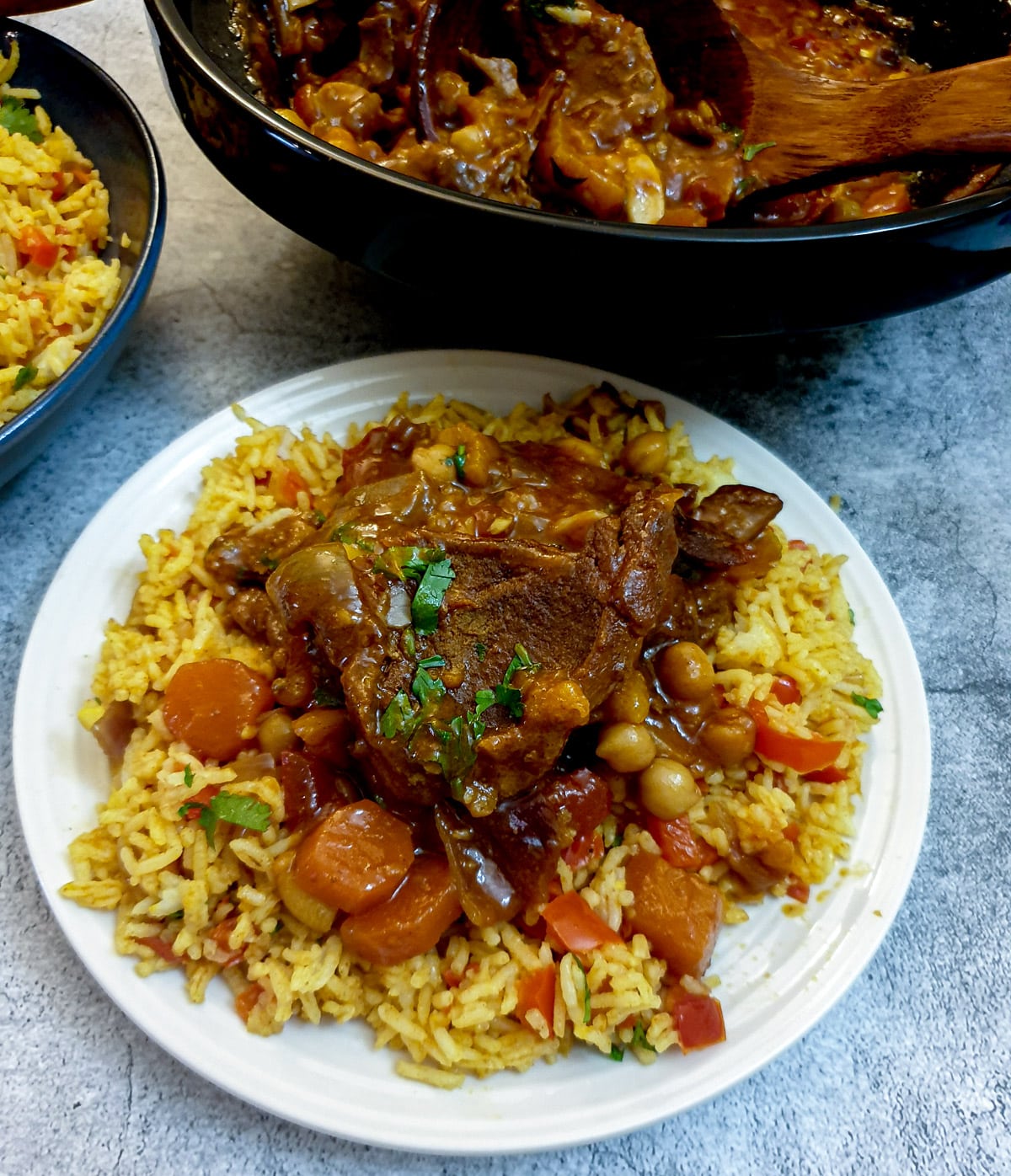 A white plate of Moroccan rice topped with lamb tagine.