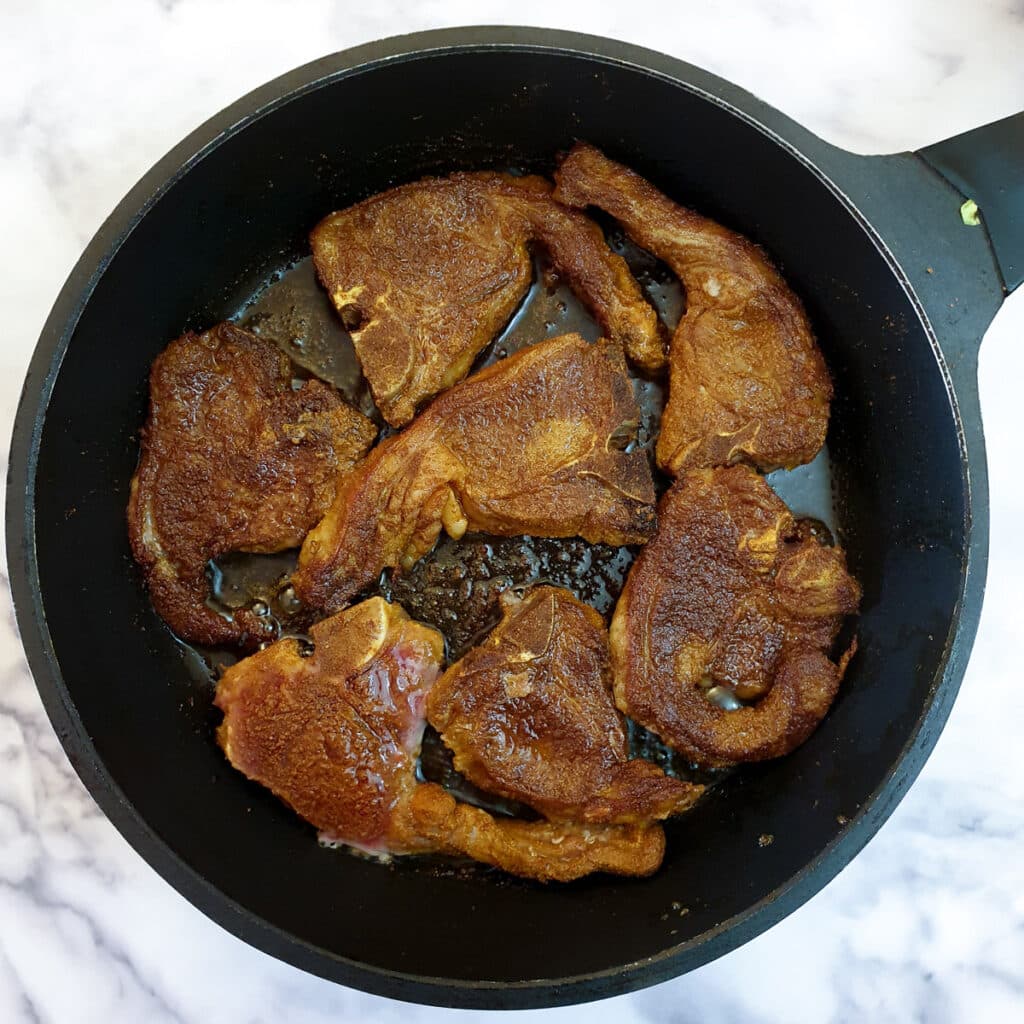 Spice coated lamb chops in a frying pan.