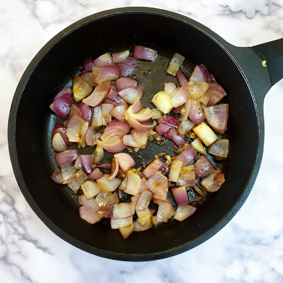 Onions and garlic softening in a frying pan.