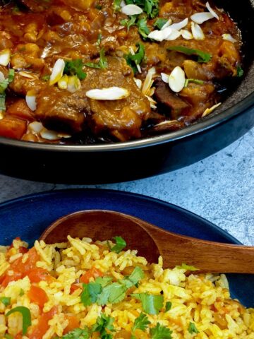 A tagine filled with Moroccan lamb stew next to a bowl of spicy rice.