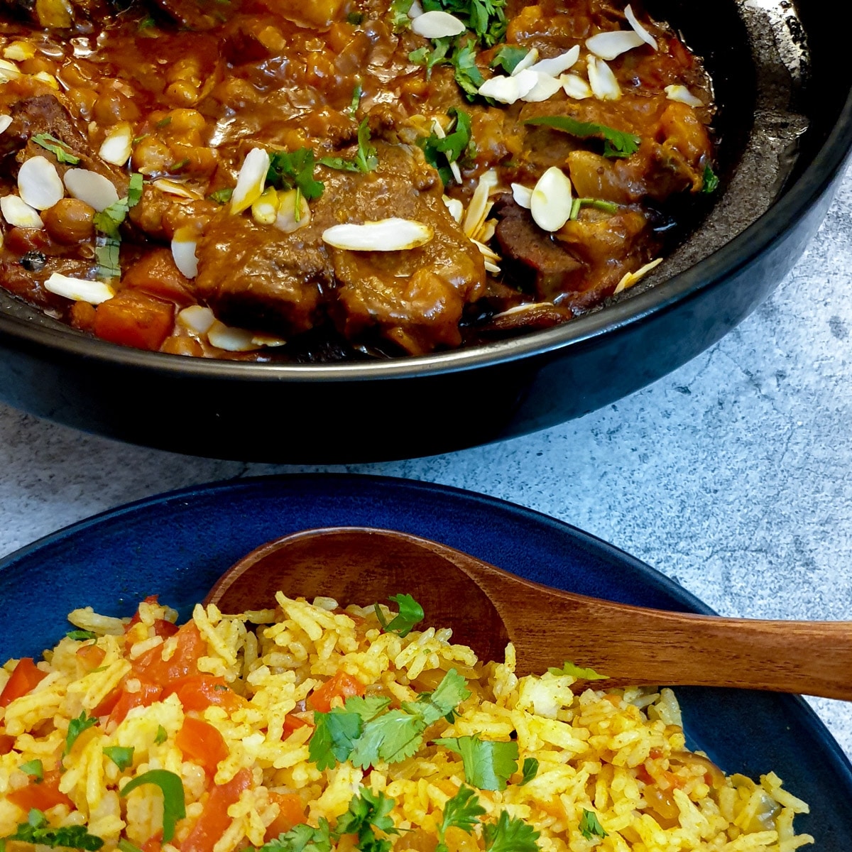 A tagine filled with Moroccan lamb stew next to a bowl of spicy rice.