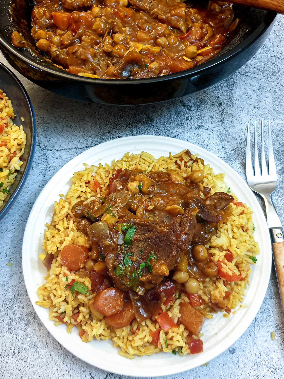 A white plate with a helping of spicy Moroccan rice topped with lamb stew.