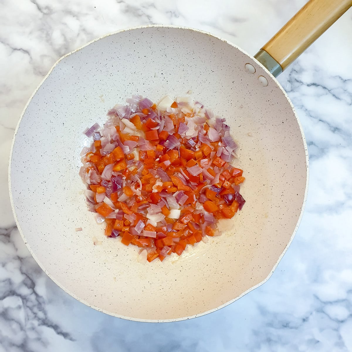 Onions and red peppers softening in oil in a wok.