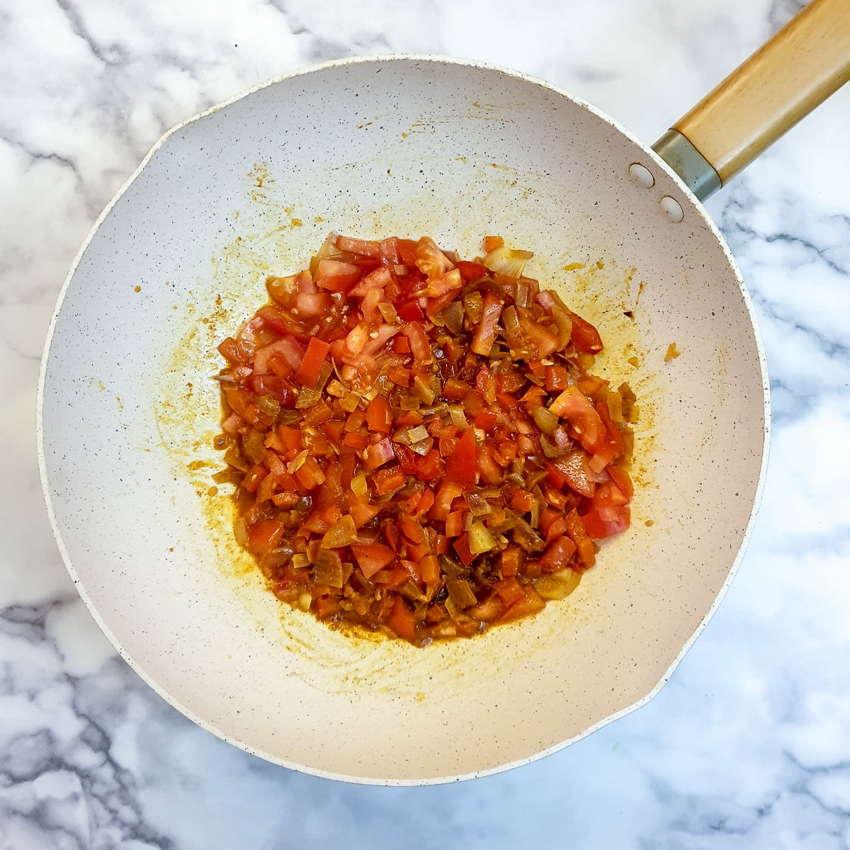 Spices and tomatoes stirred into onions and red peppers in a wok.