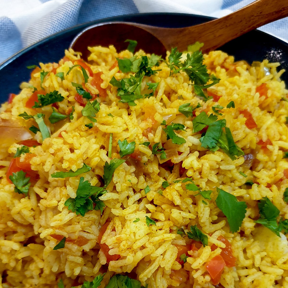 A serving dish of spicy Moroccan rice with a large wooden spoon.