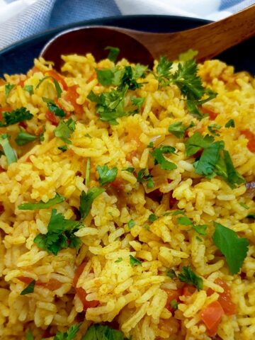 A serving dish of spicy Moroccan rice with a large wooden spoon.