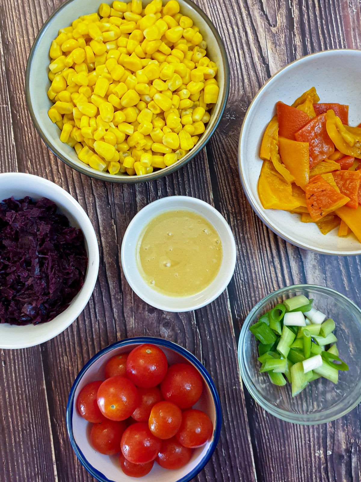 Various salad ingredients in small bowls surrounding a dish of honey mustard dressing.