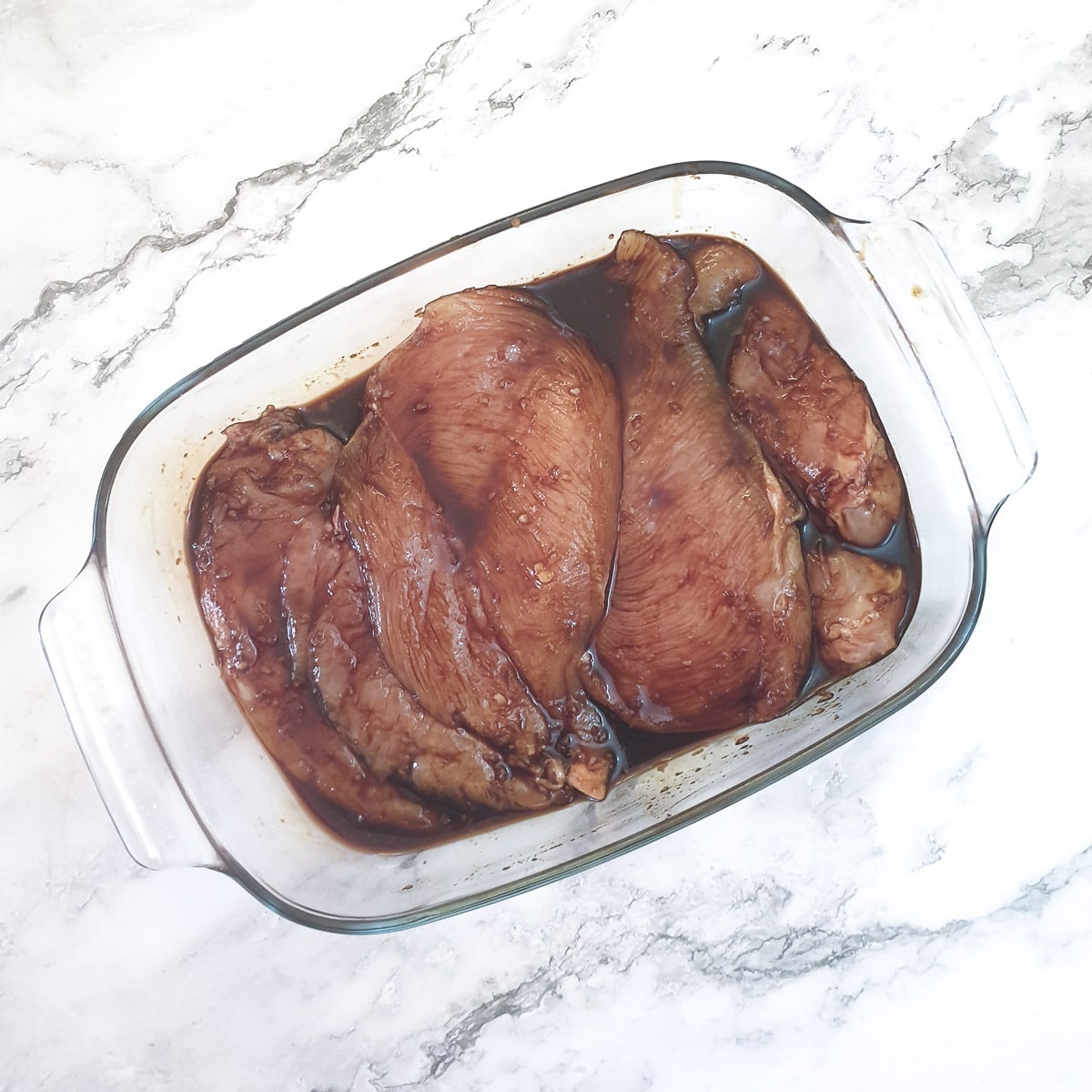 Chicken breasts in a marinade of honey, soy and garlic in a glass bowl.