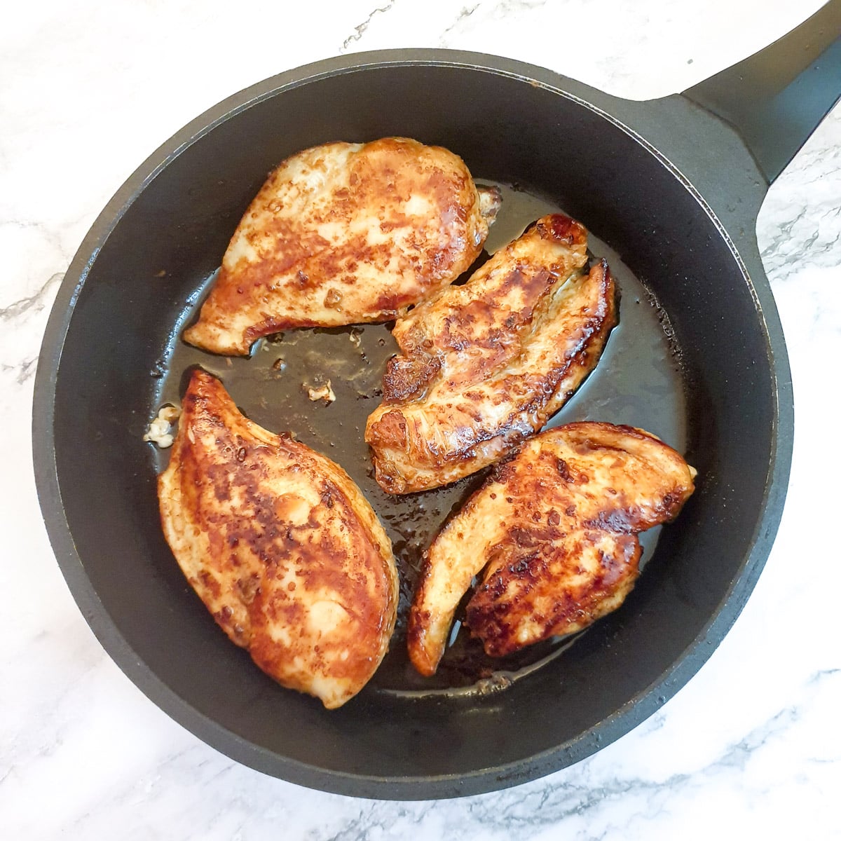 Chicken breasts browning in a frying pan.