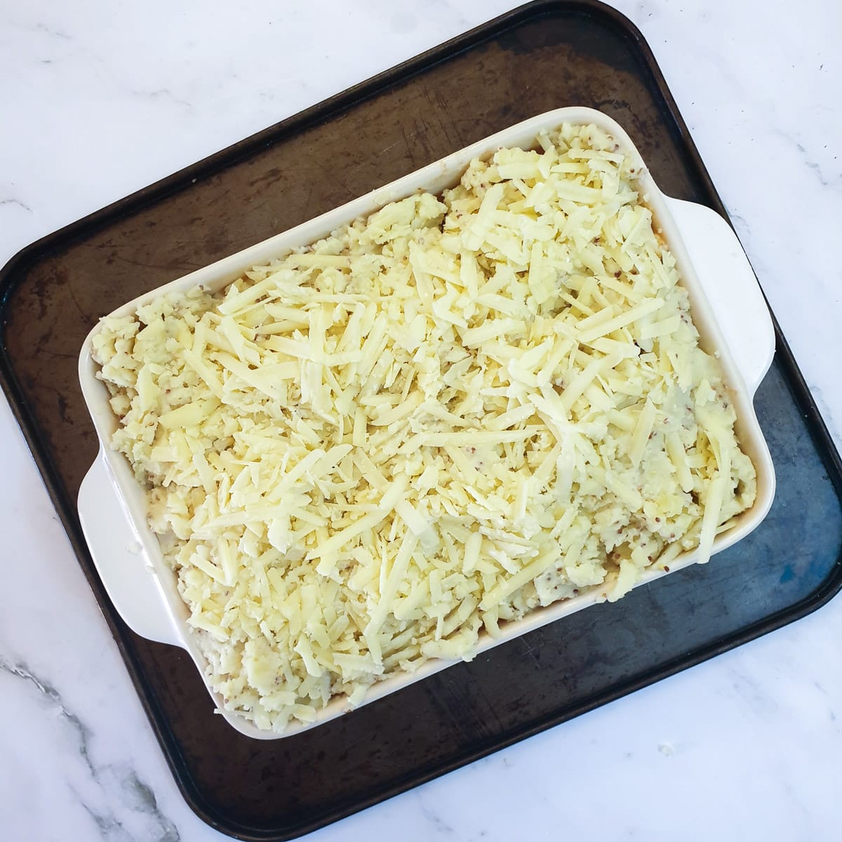 Masned potatoes and grated cheese spread over sausages in a casserole dish.