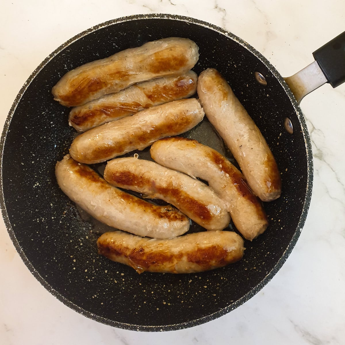 8 sausages being browned in a frying pan.