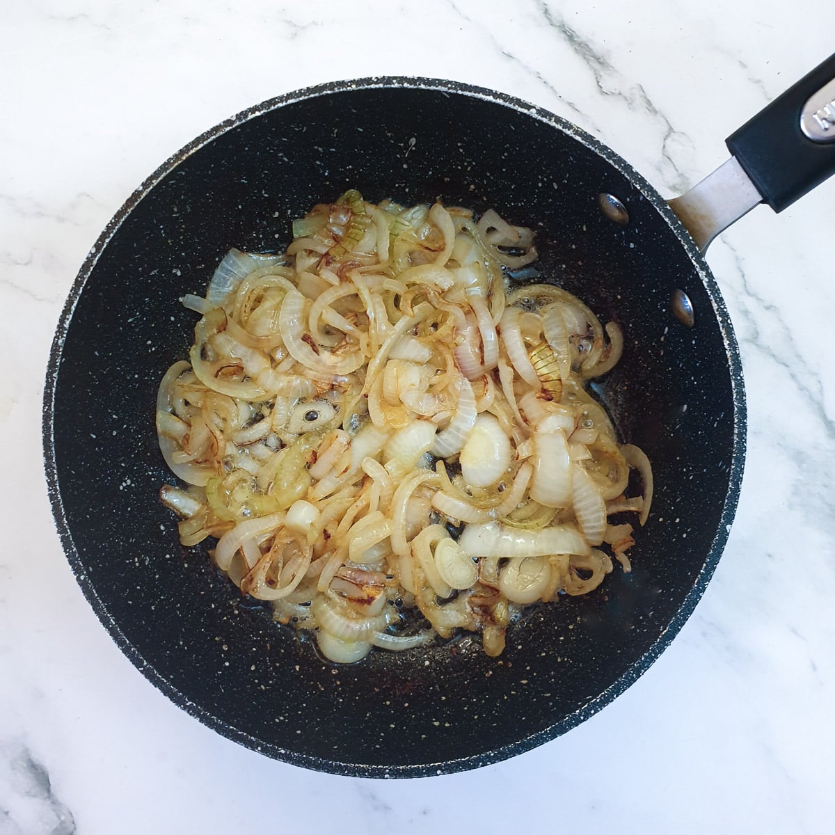 Sliced onions browning in a frying pan.