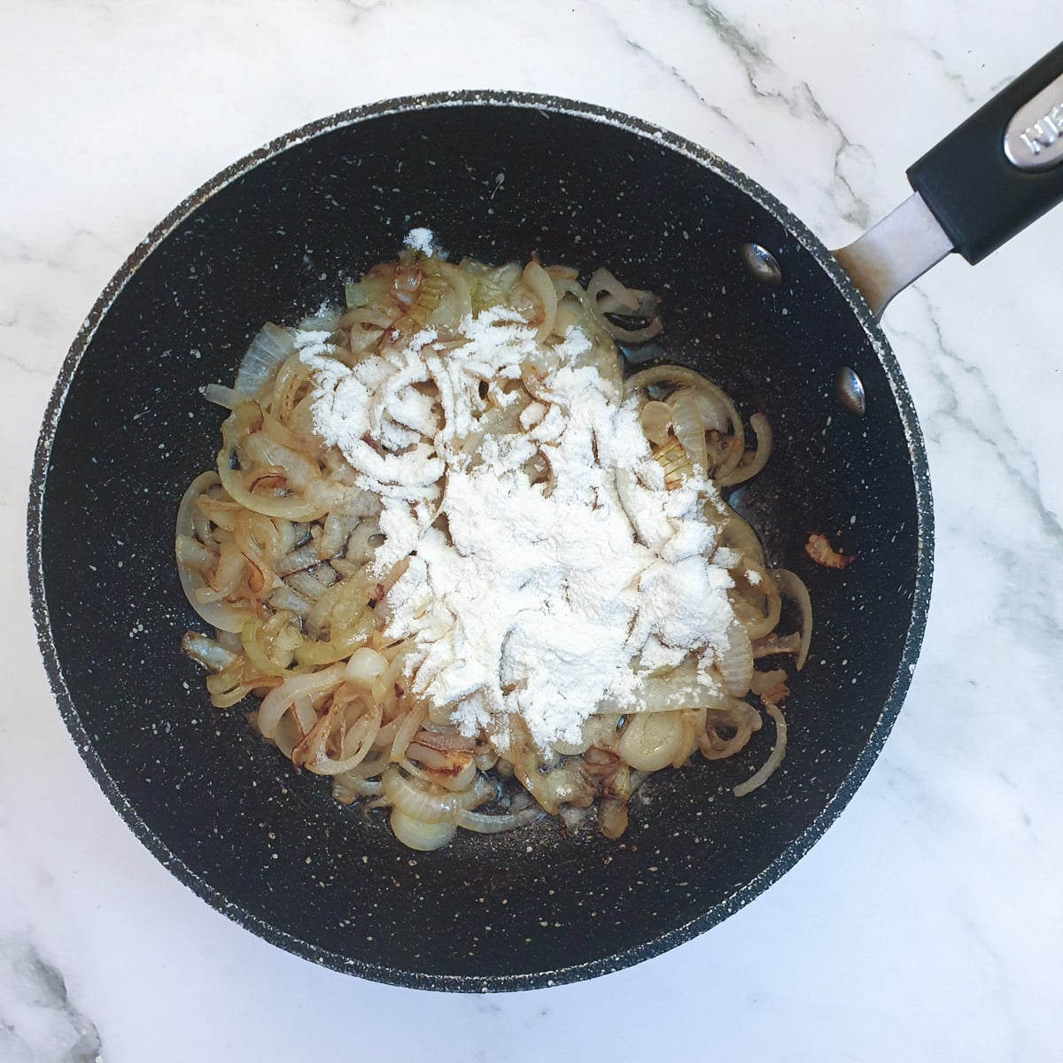 Flour sprinkled over onions in a frying pan.