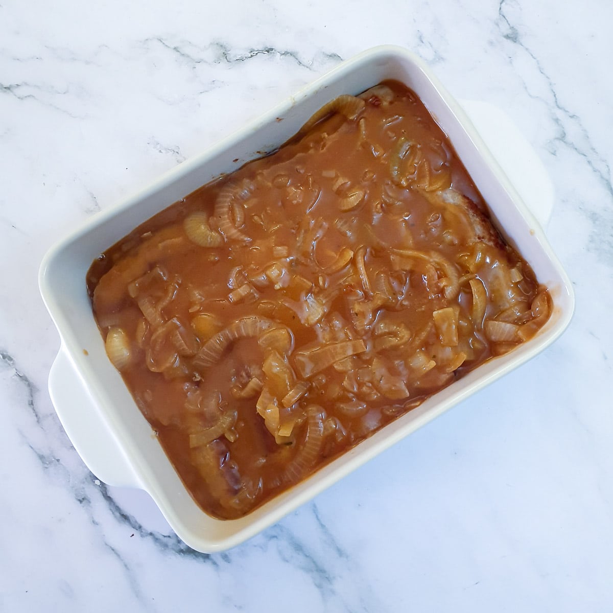 Onion gravy poured over sausages in a casserole dish.