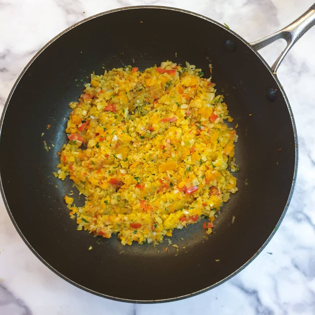 Finely chopped onions, red pepper and coriander being softened in a frying pan.