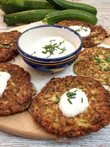 Cheese courgette fritters on a wooden board with a bowl of sour cream and chive dip.