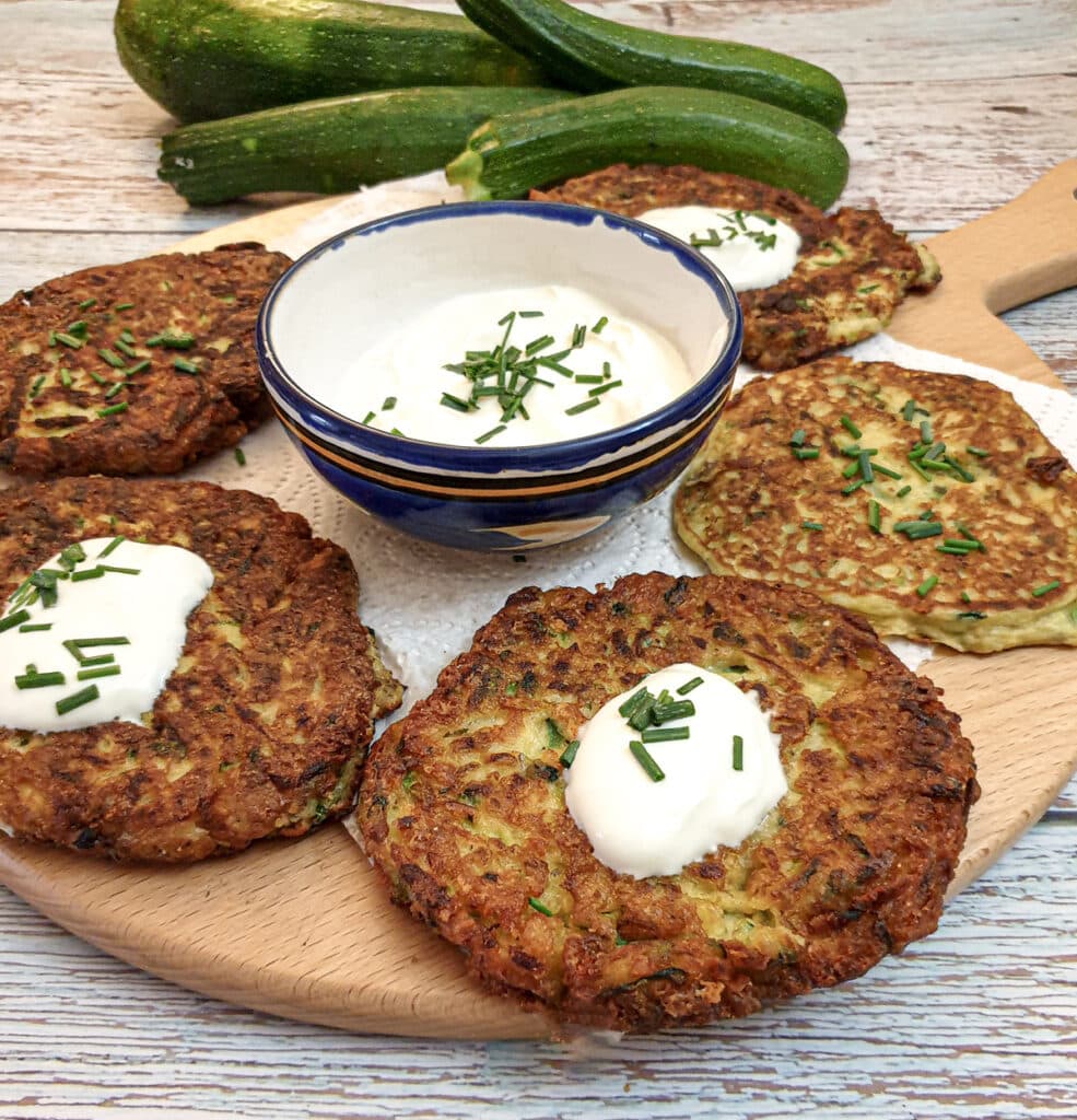 Cheesy courgette fritters on a wooden board with a bowl of sour cream and chive dip.