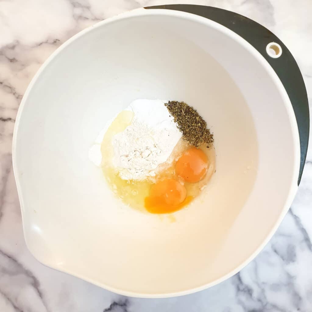 Eggs, flour and mixed herbs in a mixing bowl.