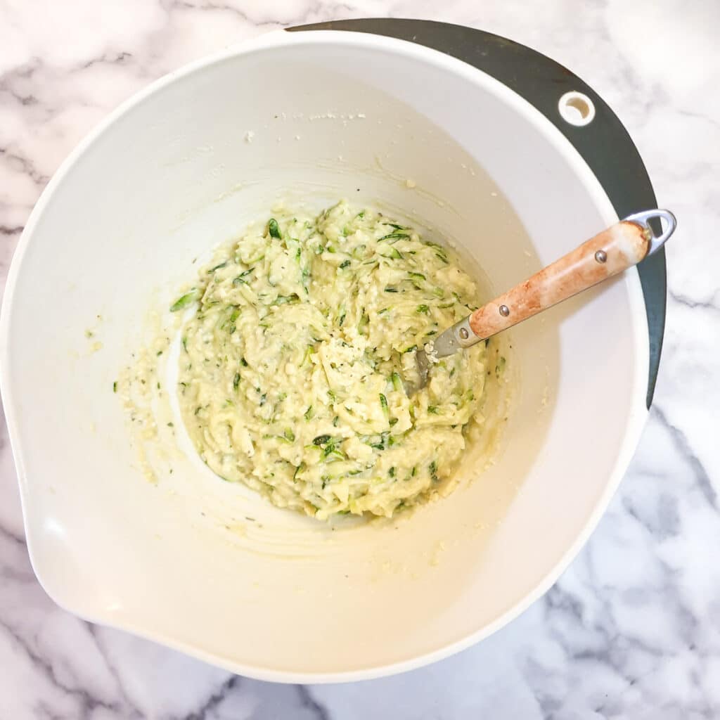 A mixing bowl containing  a batter of eggs, flour, grated courgettes and grated cheese.