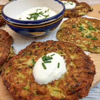 Closeup of a cheese courgette fritter topped with a spoonful of sour cream and a sprinkling of chopped chives.