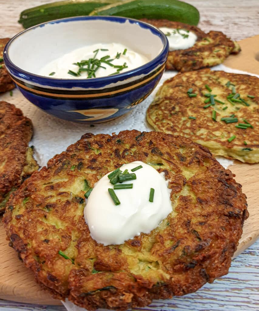 Closeup of a cheese courgette fritter topped with a spoonful of sour cream and a sprinkling of chopped chives.