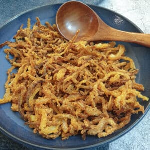 Crispy fried onions in a blue dish with a brown wooden serving spoon.