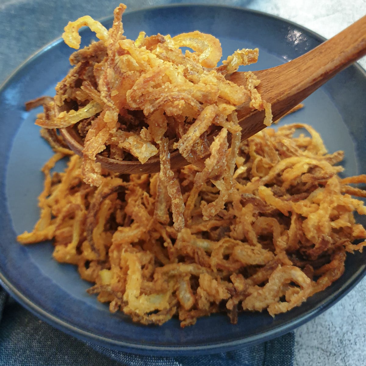 A spoonful of crispy fried onions held above a blue dish.