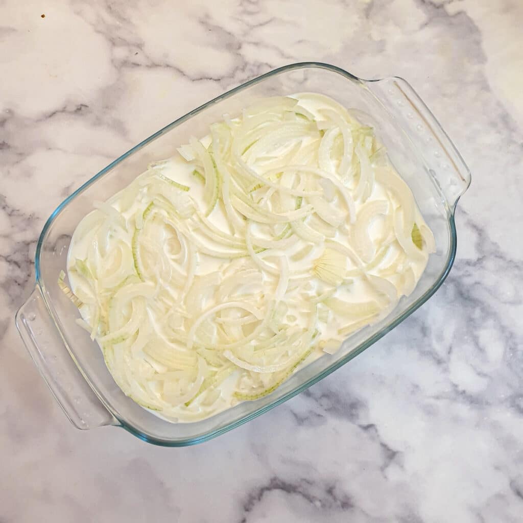 Sliced onions and buttermilk in a shallow glass dish.