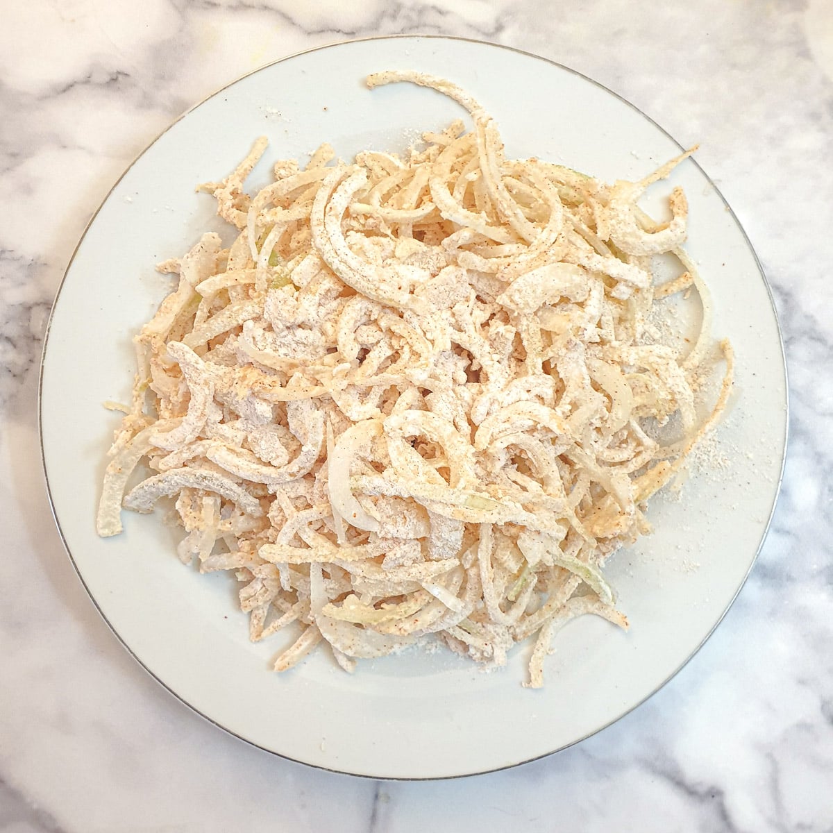 Onions coated with flour on a white plate.