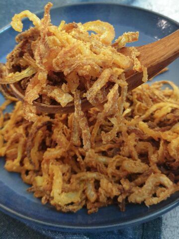 A spoonful of crispy fried onions held above a blue dish.