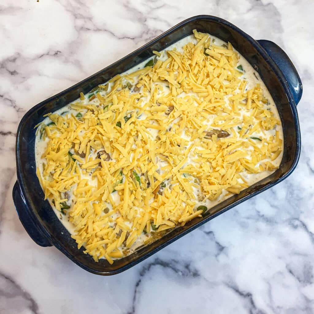 Egg custard poured over vegetables, covered with grated cheese, in a baking dish.