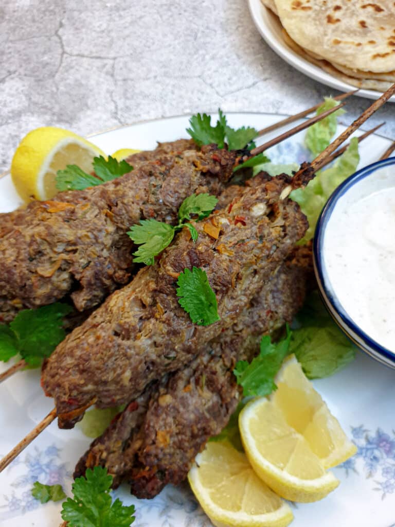 Close up of lamb kofta on a plate with slices of lemon.