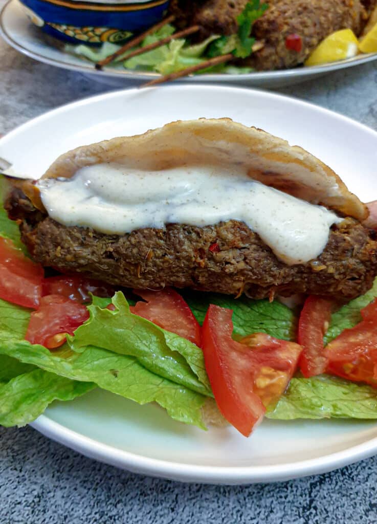 A lamb kofta in a flatbread with tomato and lettuce, and covered with spicy yoghurt dipping sauce.