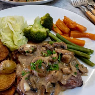 Marsala mushroom sauce poured over a steak on a plate with vegetables.