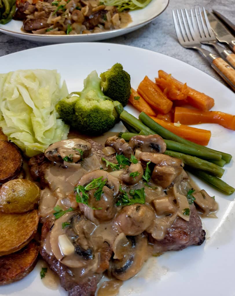 Marsala mushroom sauce poured over a steak on a plate with vegetables.