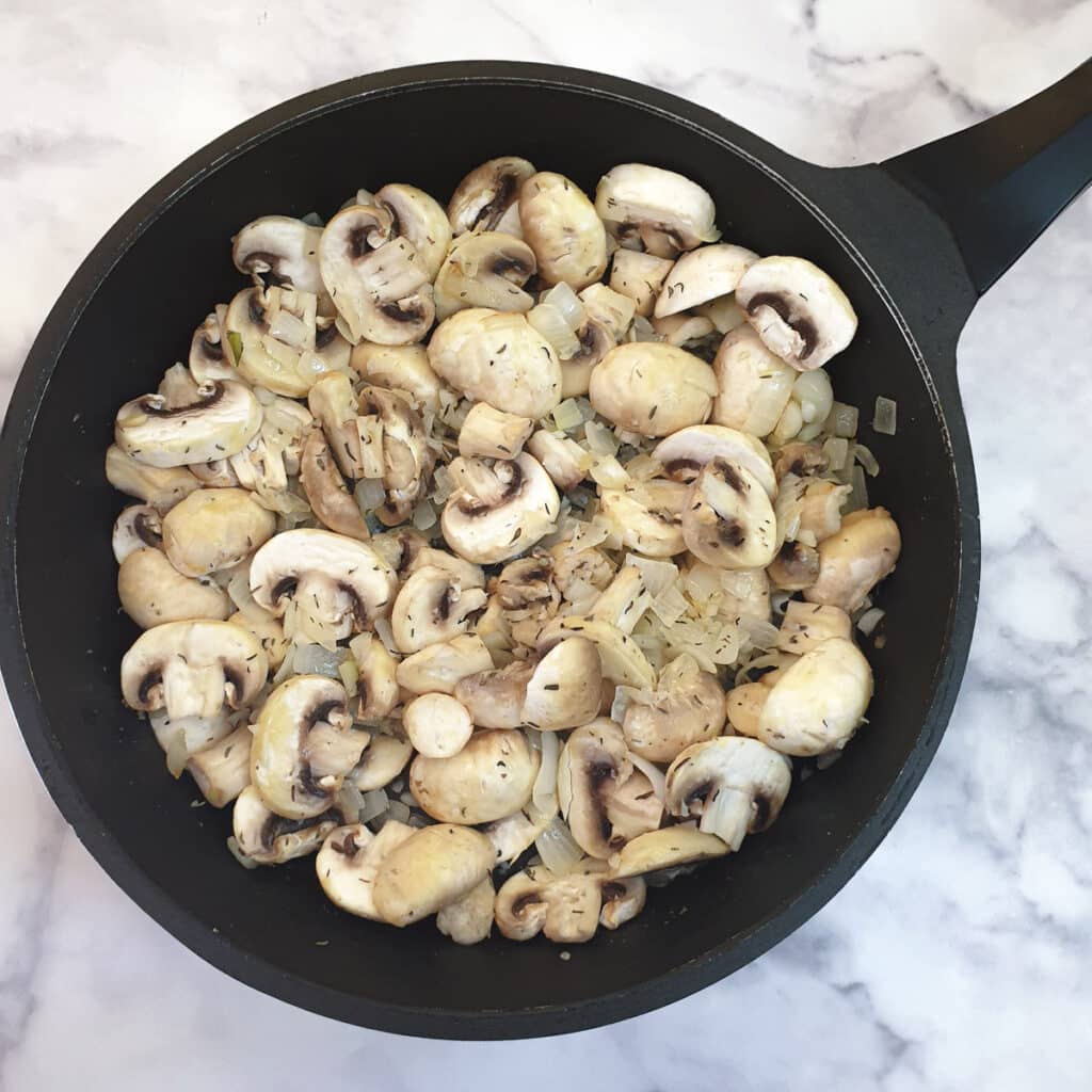 Chopped mushrooms and thyme added to onions in a frying pan.