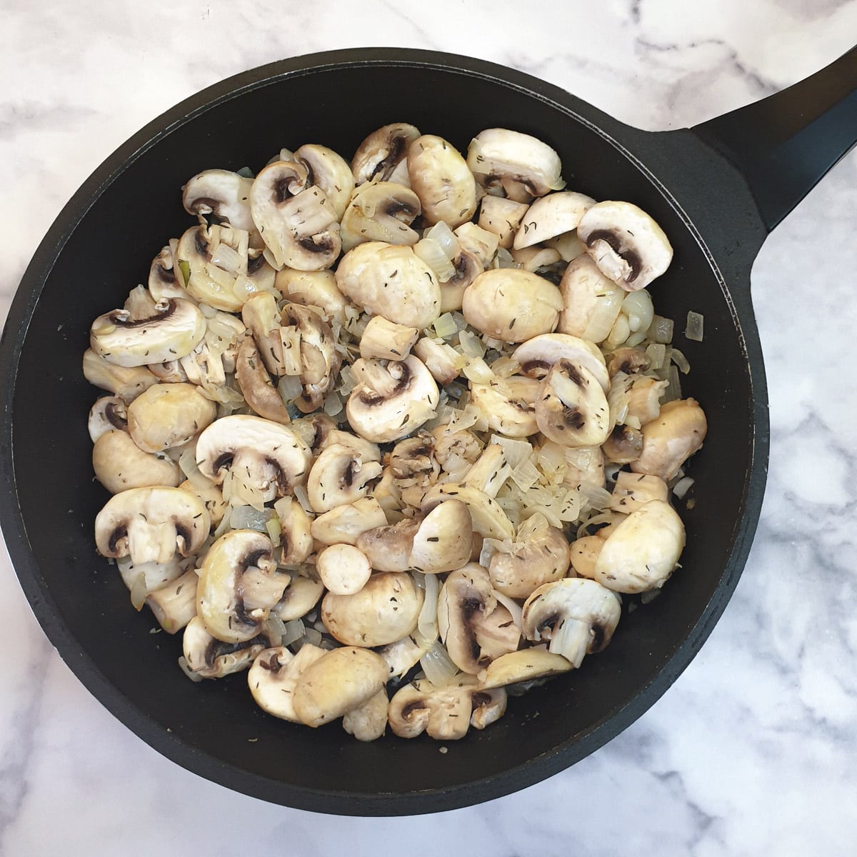 Chopped mushrooms and thyme added to onions in a frying pan.